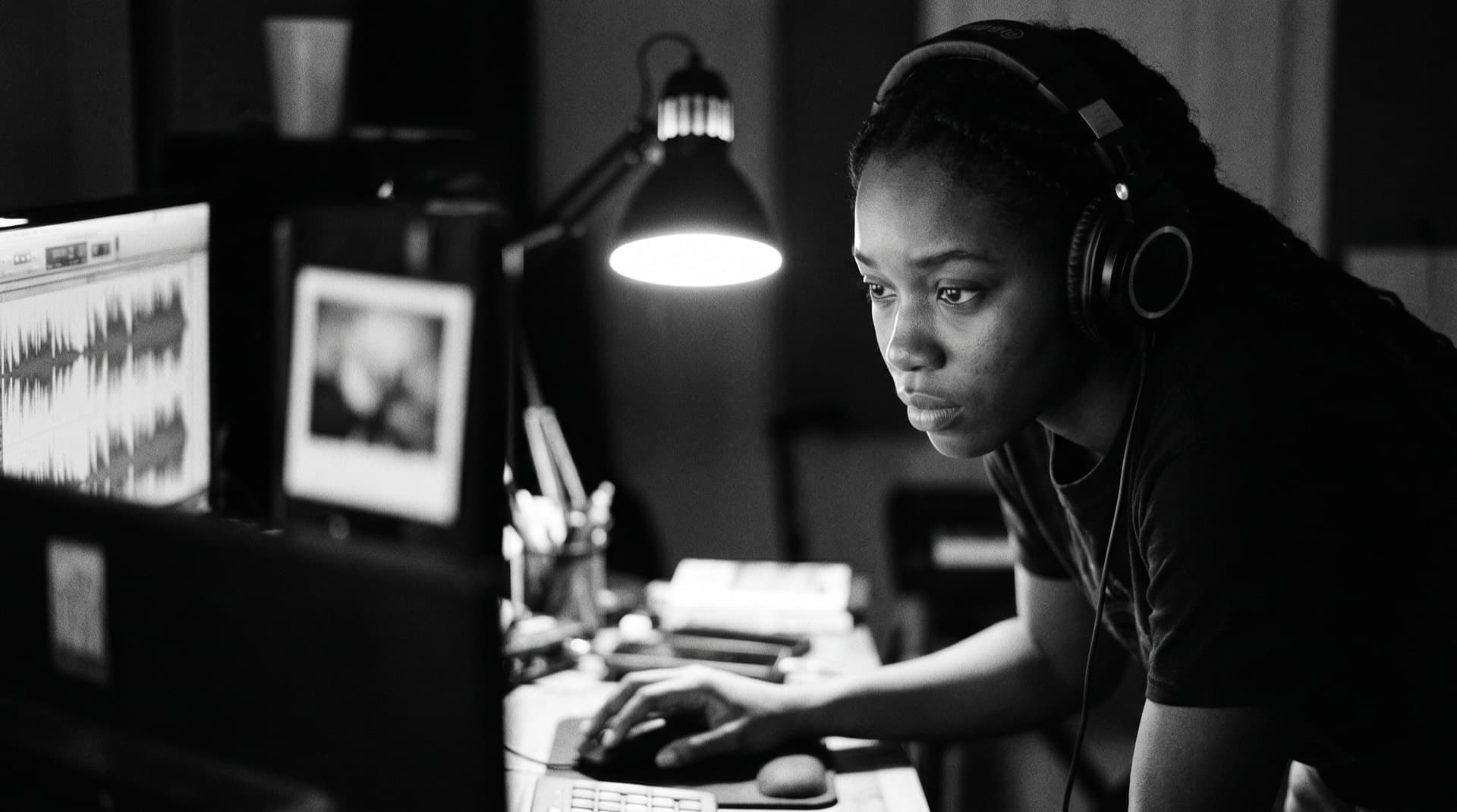 Woman in headphones annotating a screen showing an audio waveform and a photo, hand on the mouse